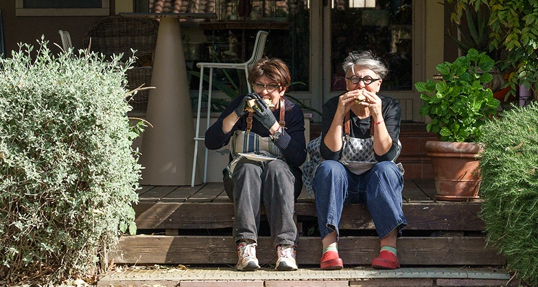Le sorelle, Francesca e Cristina, mentre addentano due panini a sedere sugli scalini della pedana in legno fuori dal ristorante da Alcide.