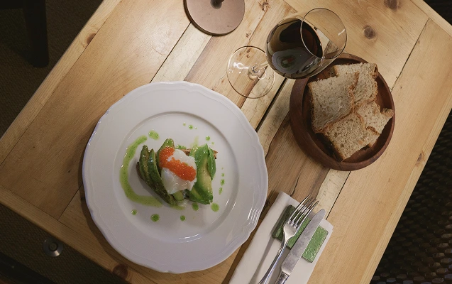 tavola_ristorante Tavola vista dall'alto con piatto avocado toast, calice di vino rosso e cesto del pane fatto in casa.